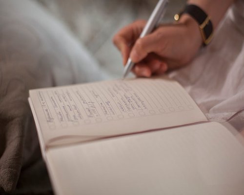 A person writing their daily routine and goals in a notebook at home